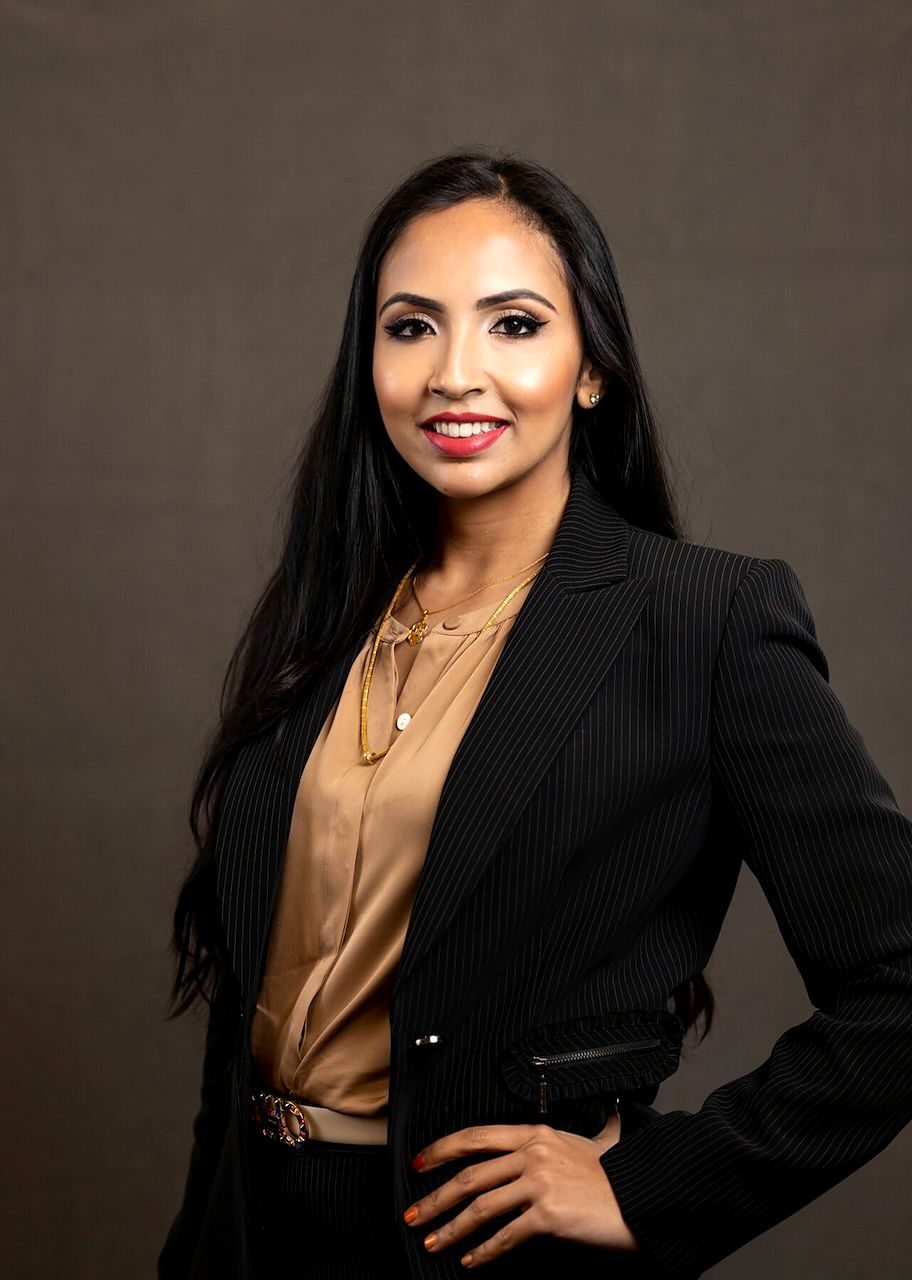 Dr. Tanzila Rahman in a black pinstripe blazer and camel silk blouse, smiling.